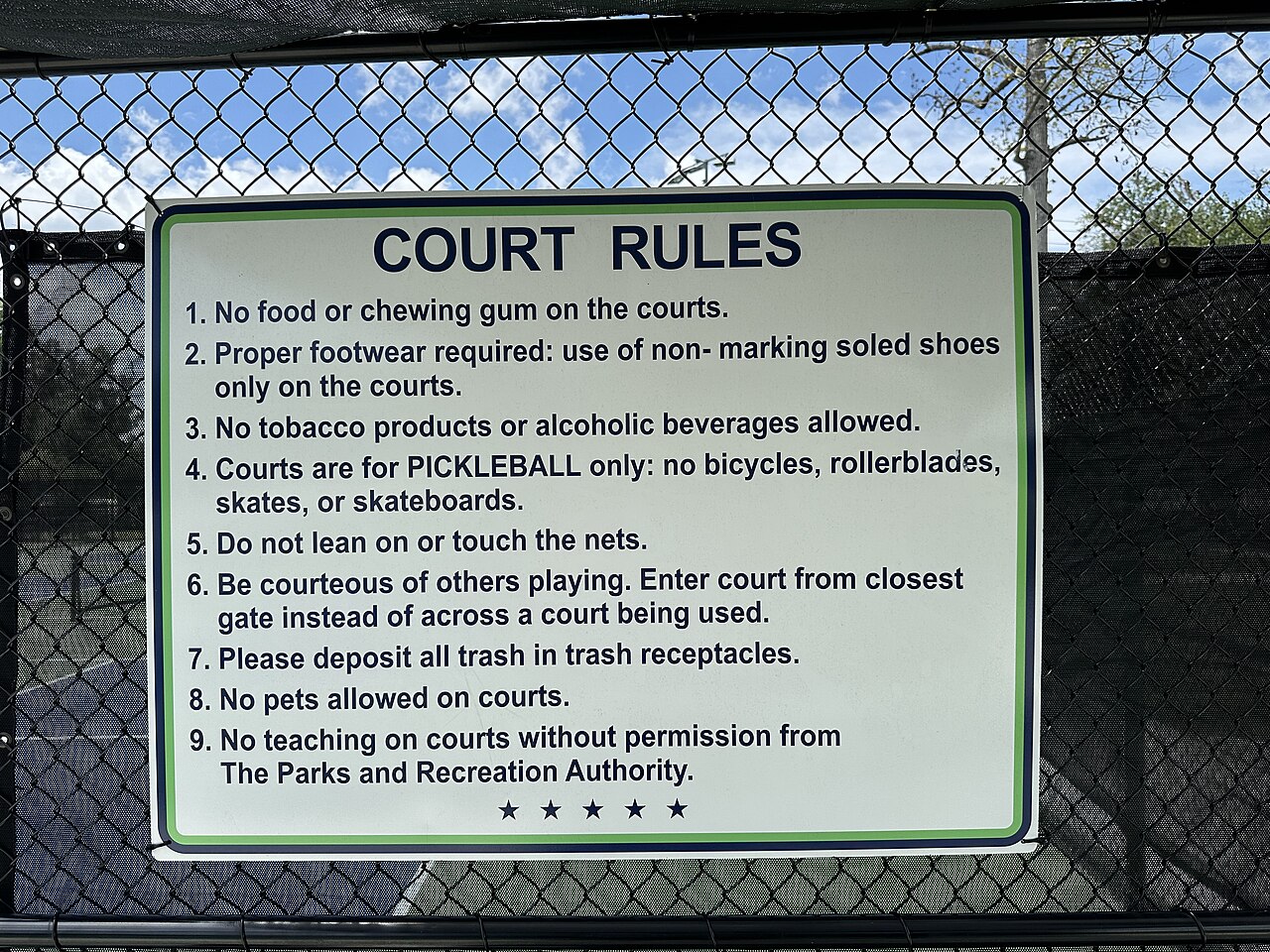 This sign is affixed to the exterior of the fence surrounding pickleball court 3 at its northeast corner. The sign displays the rules for using the pi